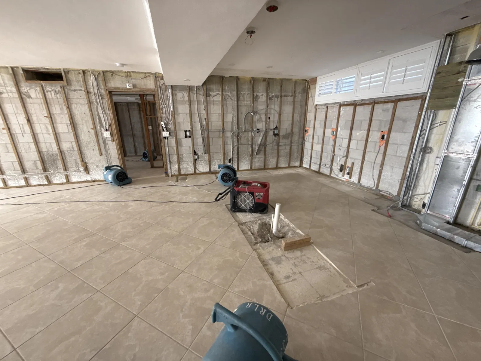 Same space after CCRS mitigation — air movers and dehumidifiers deployed, walls stripped clean, drying protocol active